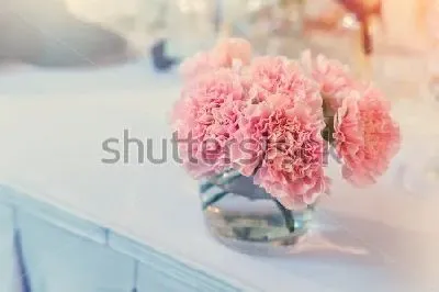 Букетик розовых гвоздик в стеклянном стакане на белой столешнице