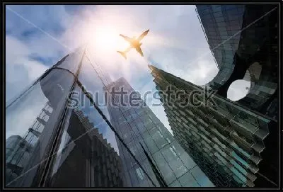 Самолёт над стеклянными небоскрёбами в лучах яркого солнца