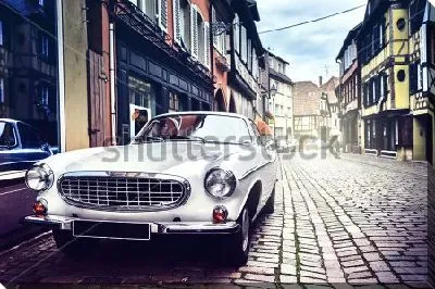 Постер Красивый белый ретро автомобиль на мощёной улице старинного европейского города