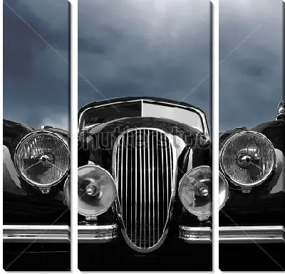 Передняя часть чёрного ретро автомобиля с фарами на фоне свинцового неба