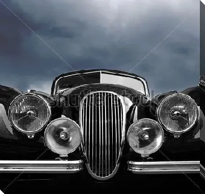 Постер Передняя часть чёрного ретро автомобиля с фарами на фоне свинцового неба