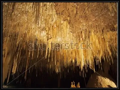Тонкие нити сталактитов в красивом золотом освещении пещеры