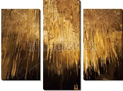 Тонкие нити сталактитов в красивом золотом освещении пещеры