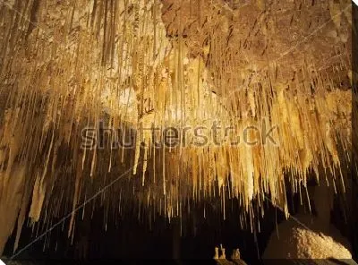 Тонкие нити сталактитов в красивом золотом освещении пещеры