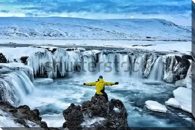 Постер Путешественник любуется величественным видом заснеженного водопада Годафосс (Исландия)