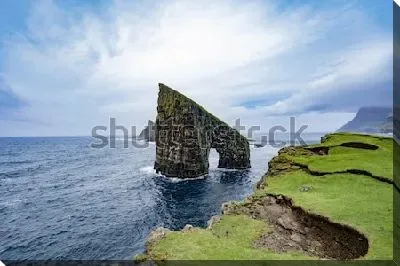 Постер Пейзаж со живописной скалой Дрангарнир в океане со стороны зелёного берега (Фарерские острова, Дания)