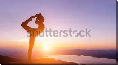 Девушка стоит на одной ноге в позе йоги на фоне красивого заката над озером и горной долиной