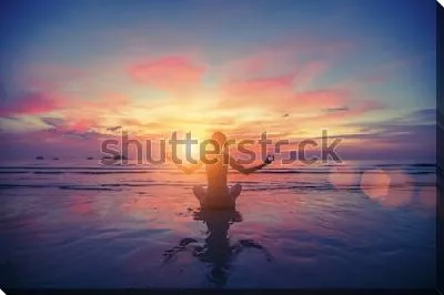 Девушка в позе лотоса медитирует на побережье океана в лучах фантастического заката