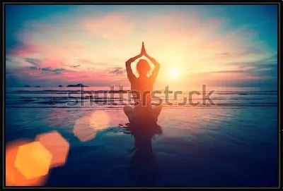 Девушка занимается йогой на берегу океана в лучах розово-золотого заката