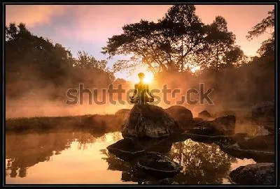 Силуэт медитирующего человека на большом камне на фоне великолепного утреннего пейзажа на берегу туманного озера