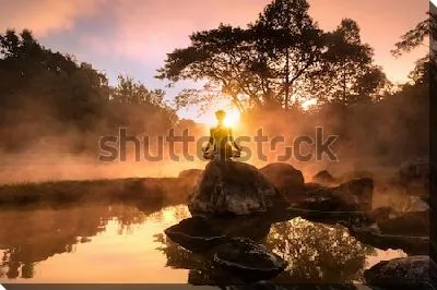 Силуэт медитирующего человека на большом камне на фоне великолепного утреннего пейзажа на берегу туманного озера