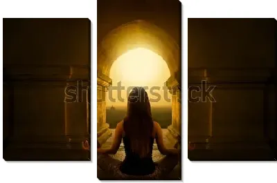 Девушка медитирует в позе лотоса под сводом арки  буддийского  храма на восходе солнца