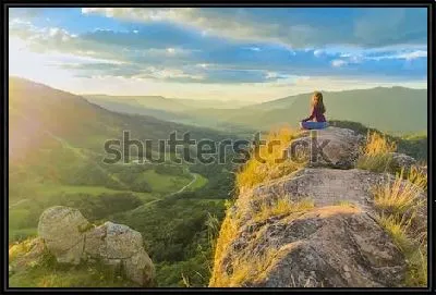 Девушка медитирует на вершине скалы с видом на великолепную горную долину в лучах рассветного солнца