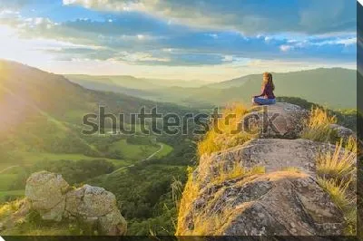 Девушка медитирует на вершине скалы с видом на великолепную горную долину в лучах рассветного солнца