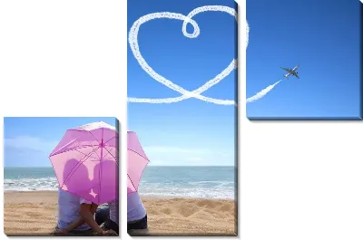 Мужчина и женщина под зонтом на берегу моря на фоне летящего самолёта вырисовывающего сердце