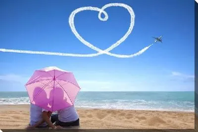 Мужчина и женщина под зонтом на берегу моря на фоне летящего самолёта вырисовывающего сердце