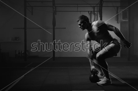 Картина Молодой мускулистый атлет выполняет упражнения с гирей в тренажёрном зале 
