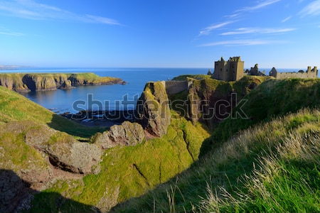 Постер Великолепный вид на замок Данноттар и скалистые холмы у моря на фоне голубого неба (Шотландия)  