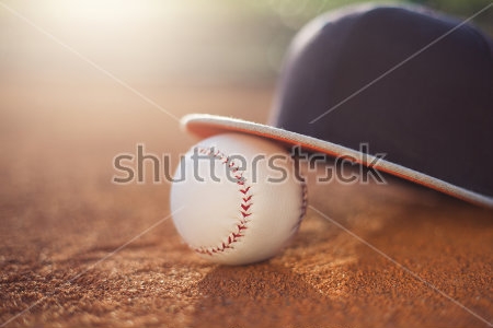Постер Бейсбольный мяч и бейсболка на игровом поле в луче солнца 