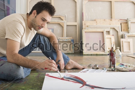 Картина Молодой человек рисует на холсте, сидя на полу в студии 
