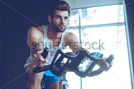 Картина Красивый молодой мужчина на велотренажёре в спортзале 
